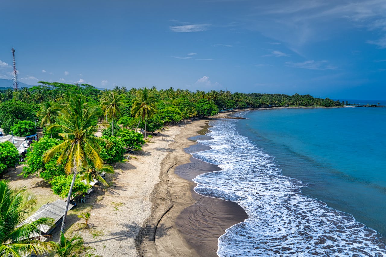 A stunning aerial view of a tropical beach in Banten, Indonesia, with clear blue skies and lush palm trees.